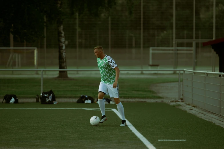 a man kicking a soccer ball on a field, during the night, evening time, in the evening