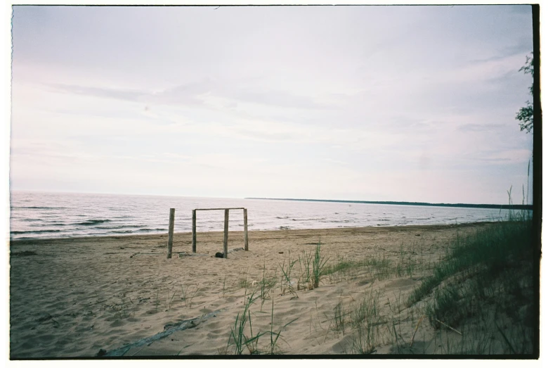 a soccer goal sitting on top of a sandy beach, a polaroid photo, by Attila Meszlenyi, land art, lake in the distance, medium format, “ iron bark, vsco film grain