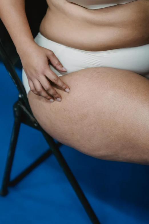 a woman in a white bikini sitting on a chair, by Elsa Bleda, unsplash, massurrealism, thick thighs, swollen muscles, blue undergarments, three hairy fat cave people