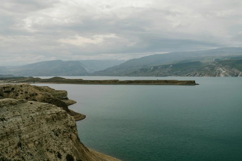 a man standing on top of a cliff next to a body of water, by Muggur, pexels contest winner, les nabis, erosion algorithm landscape, overcast lake, panels, drumheller