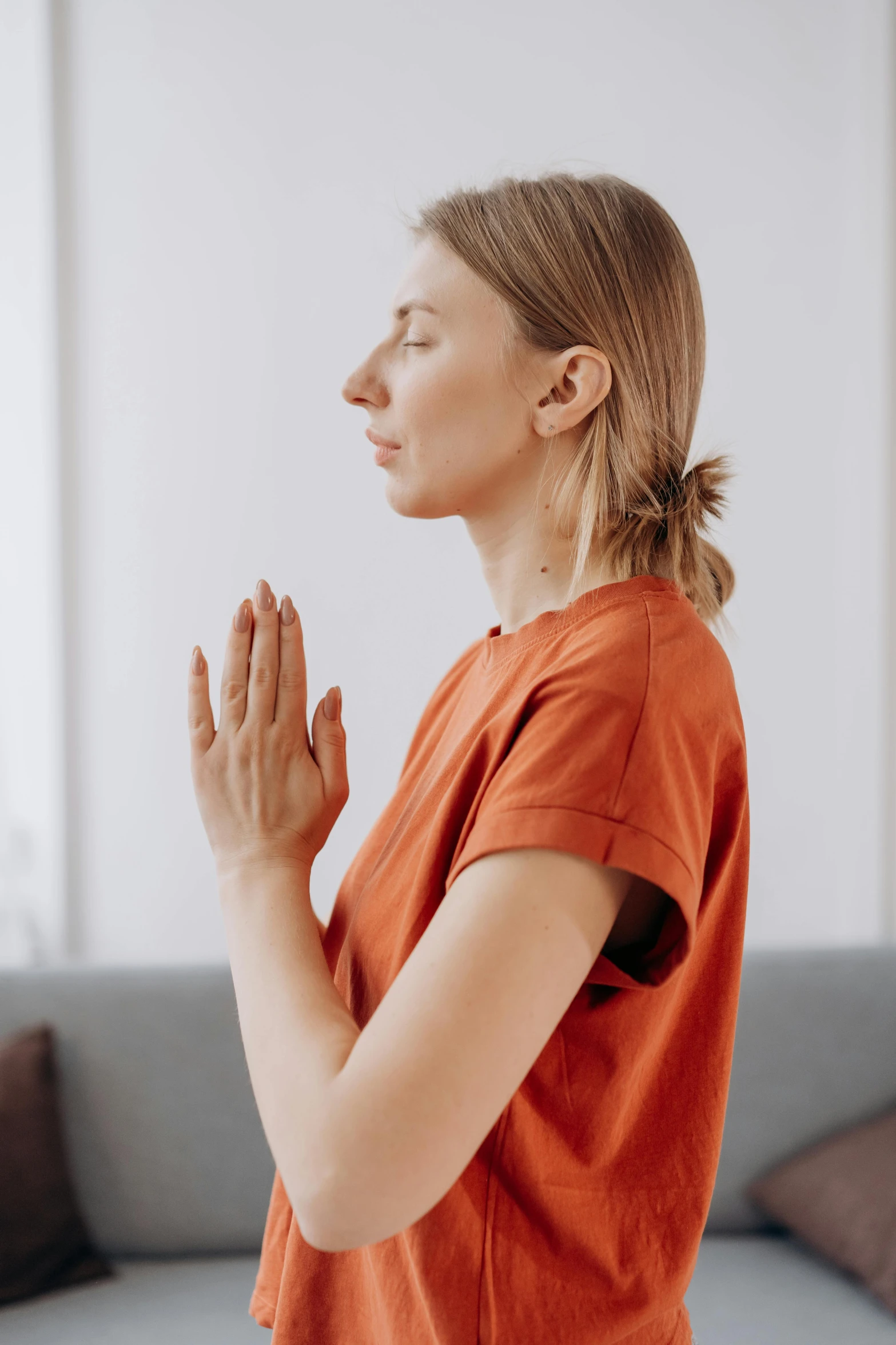 a woman in an orange shirt is doing yoga, trending on pexels, renaissance, praying posture, looking left, relief, professional photo