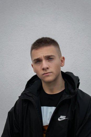 a young man standing in front of a white wall, by Attila Meszlenyi, featured on reddit, short hair on sides of head, chav, rugged face, official photo