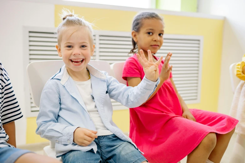 a group of children sitting next to each other, waving hands, school curriculum expert, thumbnail, two girls