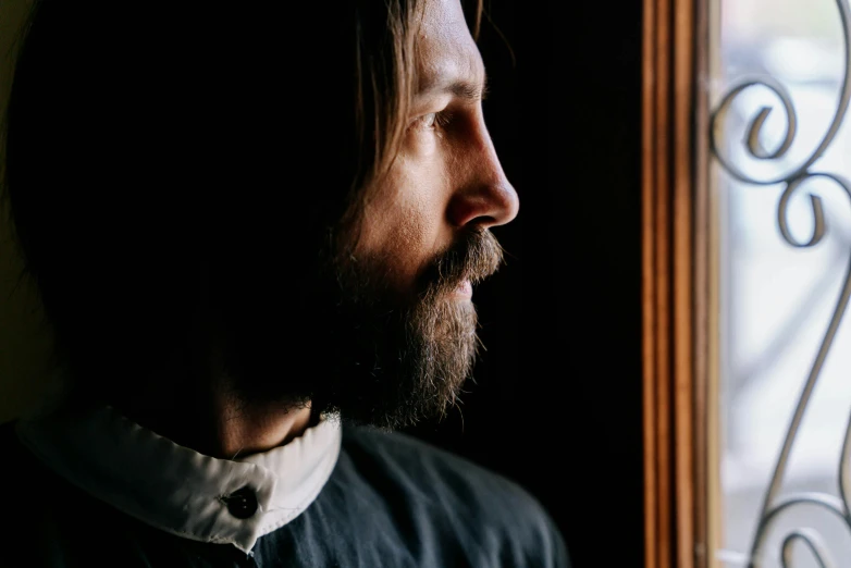 a man with long hair looking out a window, inspired by Vasily Perov, unsplash, short dark blond beard, christian saint, profile image, about to enter doorframe