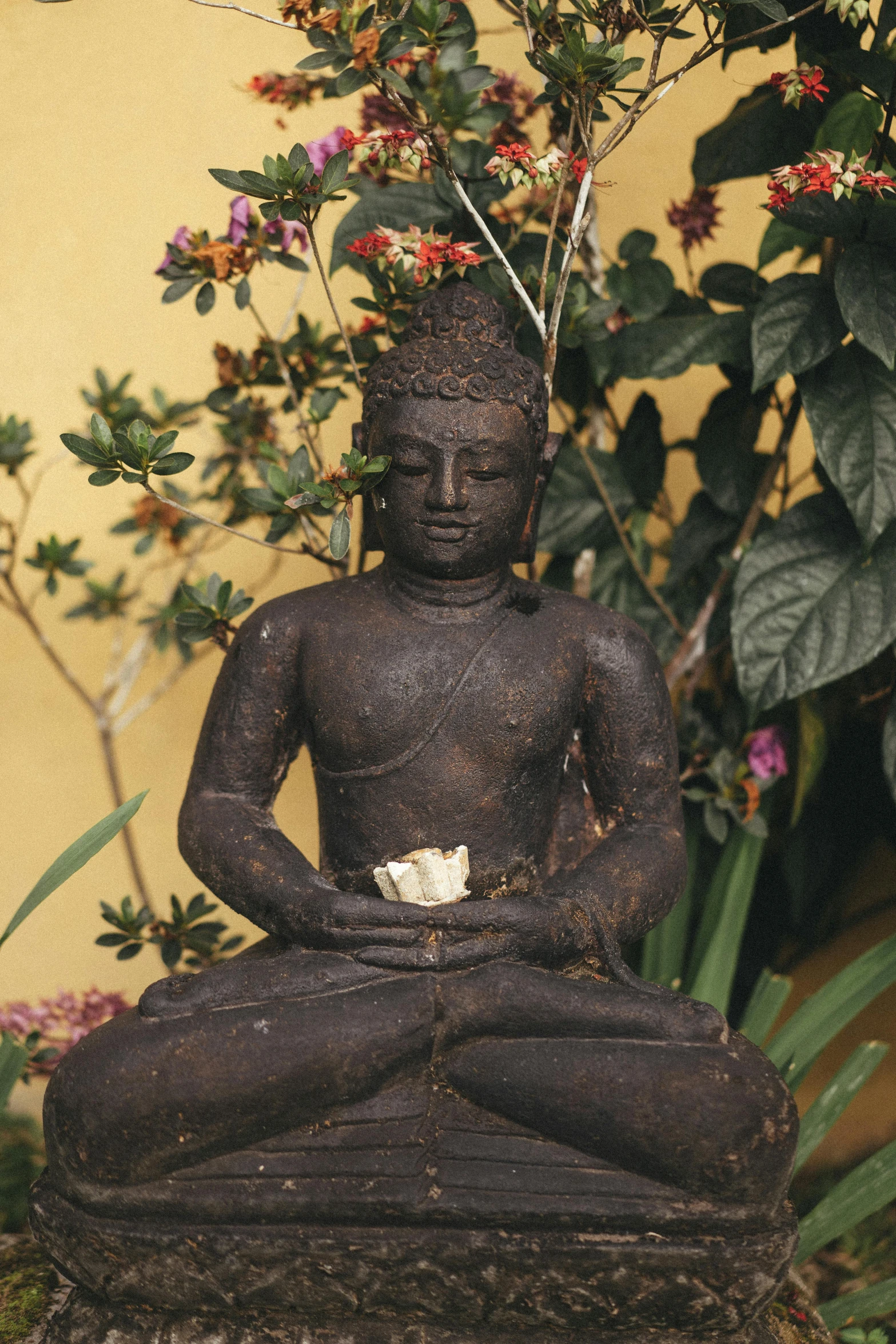 a statue of a person sitting in a lotus position, holding a flower, garden setting, indoor setting, indigo