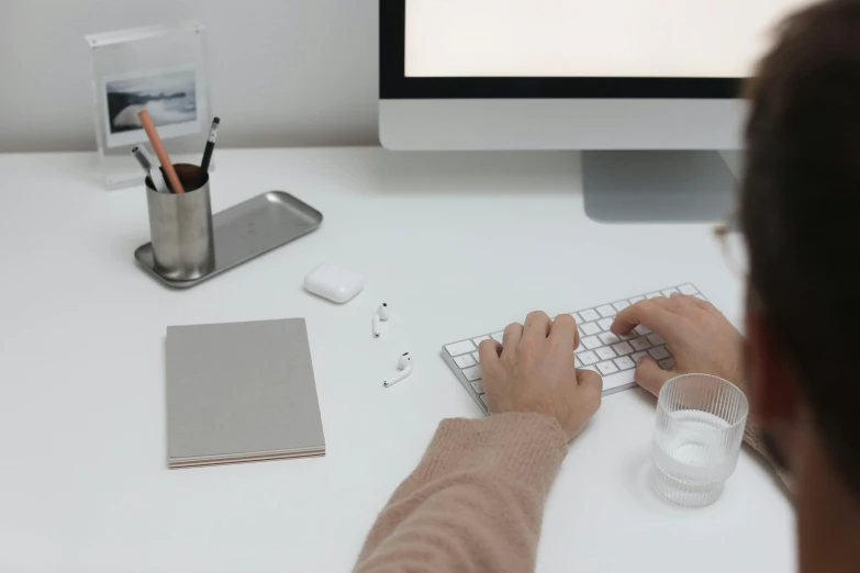 a man sitting at a desk typing on a keyboard, trending on pexels, minimalist photorealist, background image, white table, simple aesthetic