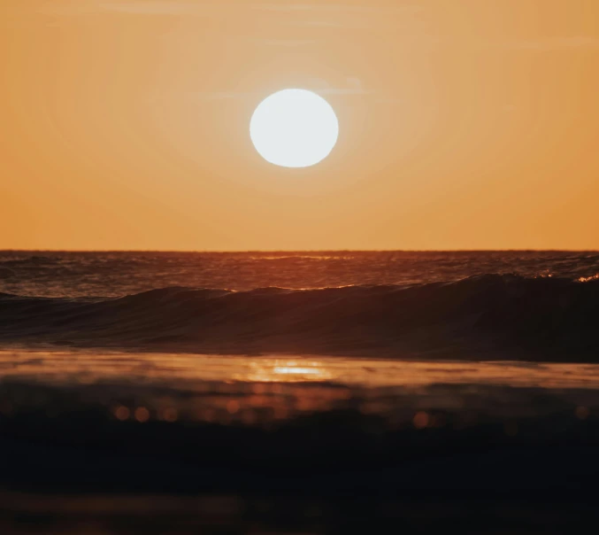 a person riding a surfboard on top of a wave, pexels contest winner, romanticism, an expansive view of the sun, orange glow, slightly pixelated, on the beach during sunset