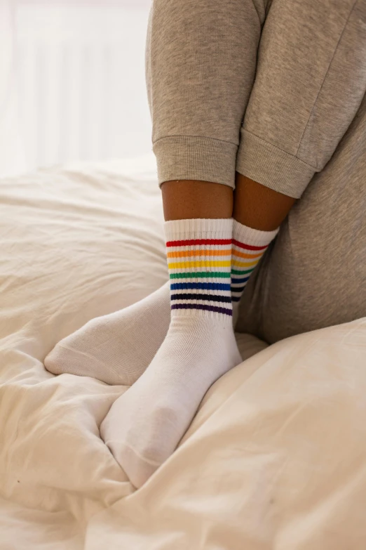 a person sitting on a bed with a pair of socks, inspired by Okuda Gensō, unsplash, renaissance, white, close up front view, young teen, muted rainbow tubing
