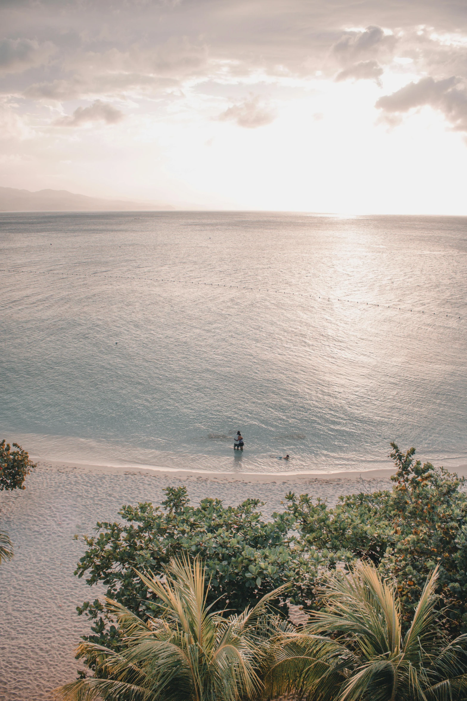 a person standing on a beach next to a body of water, lush surroundings, the ocean, evening time, overhead sun