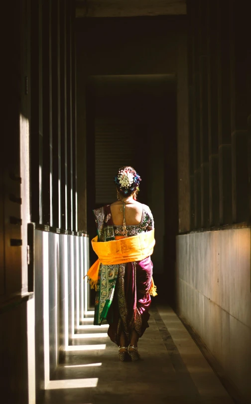 a woman walking down a hallway in a building, inspired by Steve McCurry, unsplash, wearing a colorful yukata, behind bars, indonesia, back lit