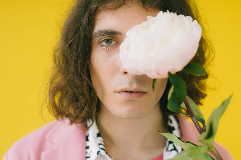 a man holding a flower in front of his face, an album cover, inspired by Syd Barrett, trending on pexels, magic realism, robert sheehan, wearing a light - pink suit, large bushy eyebrows, close up portrait photo