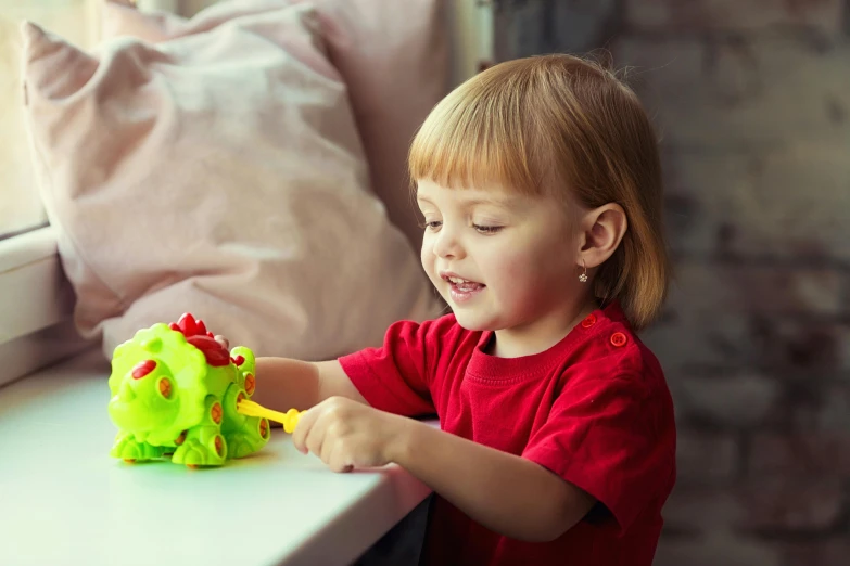 a little girl playing with a toy on a window sill, process art, green dragon, play - doh, vibrant red and green colours, mechanical frog