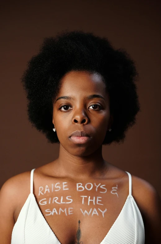 a woman with the words rise boys and girls the same way written on her chest, an album cover, by Lily Delissa Joseph, trending on unsplash, feminist art, light skinned african young girl, white ribbon, hyper realistic”, 2 0 1 5