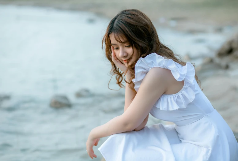 a woman in a white dress sitting on a rock by the water, inspired by Kim Du-ryang, pexels contest winner, romanticism, girl cute-fine-face, dressed in a frilly ((ragged)), japanese woman, simple stylized