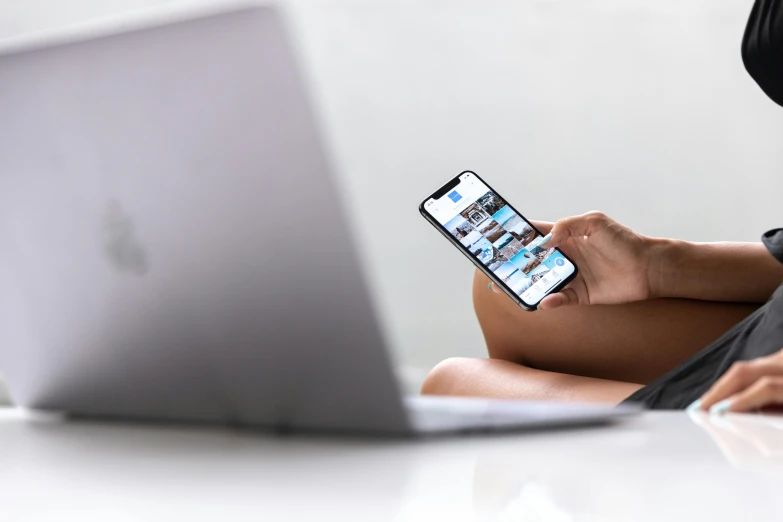 a woman sitting in front of a laptop holding a cell phone, a picture, trending on pexels, iphone 13, white backround, bottom angle, blurred