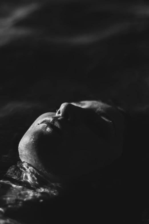 a black and white photo of a woman floating in the water, inspired by Elsa Bleda, unsplash, dark face, asleep, my blood is boiling, sad man