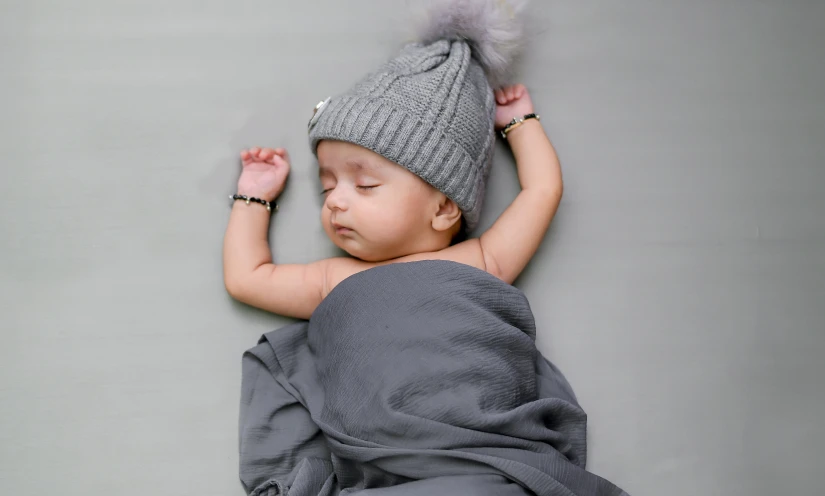 a baby wrapped in a blanket and wearing a hat, trending on pexels, symbolism, grey metal body, laying down, silver accessories, cute young man