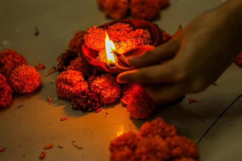a person lighting a candle on a table, kali, orange flowers, profile image, torchlights