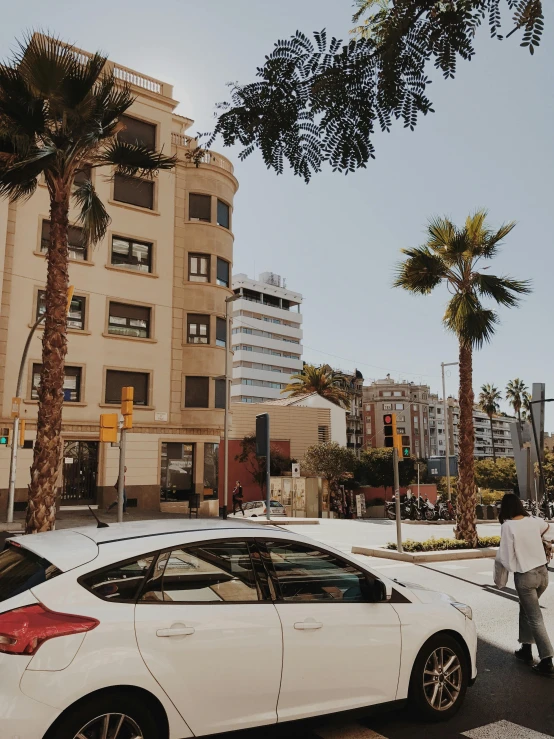 a white car driving down a street next to tall buildings, by Matija Jama, palm trees outside the windows, in spain, low quality photo, stacked image
