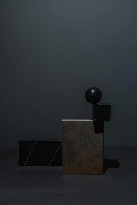 a sculpture sitting on top of a wooden block, an abstract sculpture, by Harvey Quaytman, unsplash, flying black marble balls, dark and moody colors, square shapes, 2010s