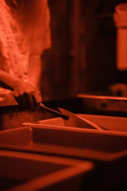 a close up of a person cutting food with a knife, a silk screen, at night, vessels, sink, reddish lighting