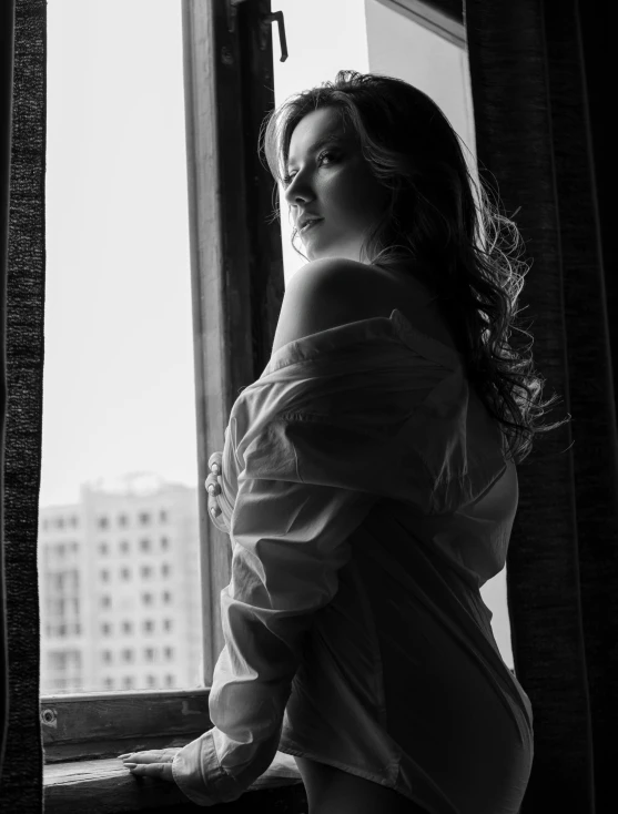 a black and white photo of a woman looking out a window, a black and white photo, by Dimitre Manassiev Mehandjiysky, art photography, young sexy elegant woman, cinematic. by leng jun, set photo, city morning