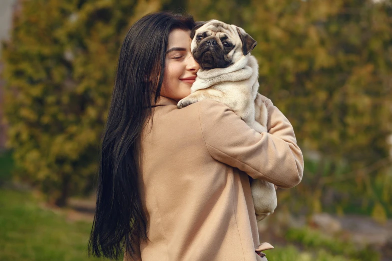 a woman holding a small dog in her arms, a picture, shutterstock, pug, mia khalifa, beige, spring season
