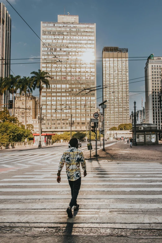 a person walking across a crosswalk in a city, by Sam Dillemans, pexels contest winner, jair bolsonaro, outdoors tropical cityscape, square, high quality photo