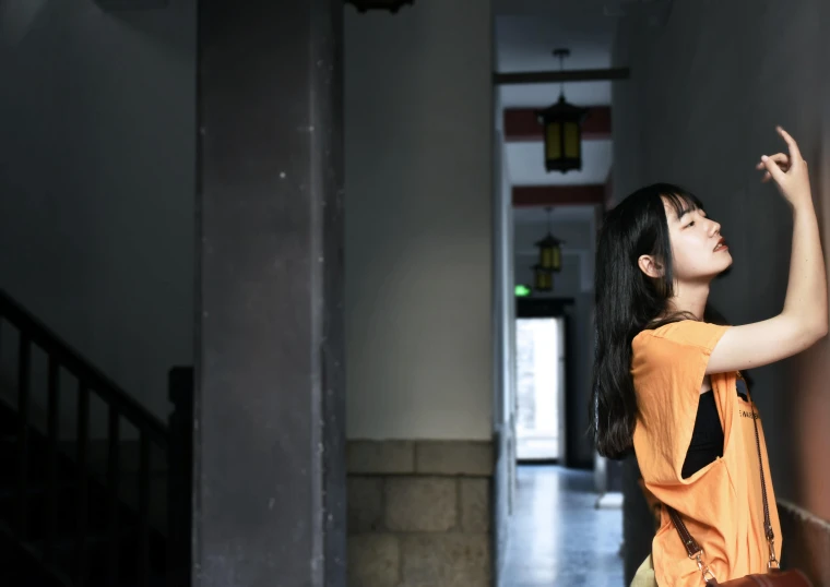 a woman in an orange shirt leaning against a wall, inspired by Tang Yifen, pexels contest winner, girl under lantern, background image, about to enter doorframe, cinematography photo