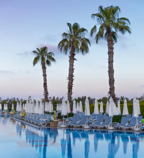 an outdoor swimming pool with lounge chairs and umbrellas, by Daniel Gelon, sunset panorama, byzantine, palm trees, shot on sony a 7