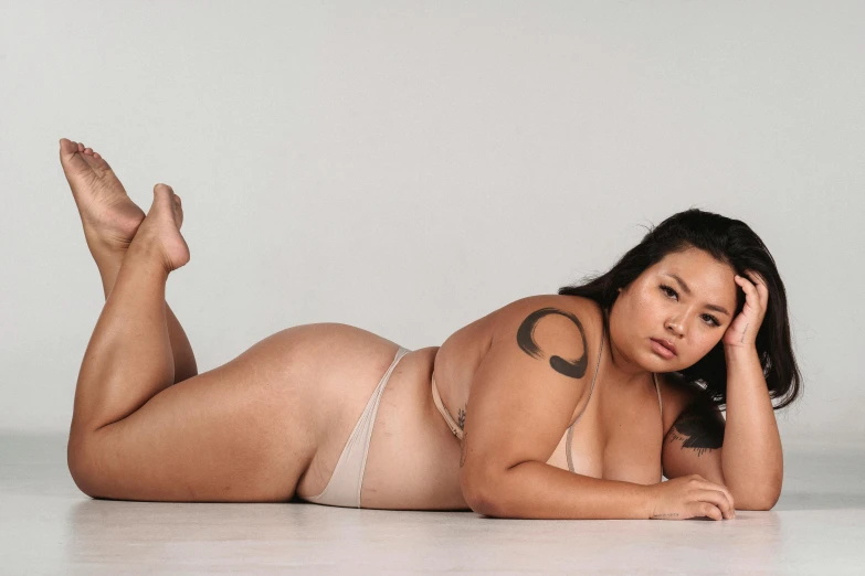 a woman in a bikini laying on the floor, unsplash, hyperrealism, obese ), half asian, non binary model, her skin is light brown