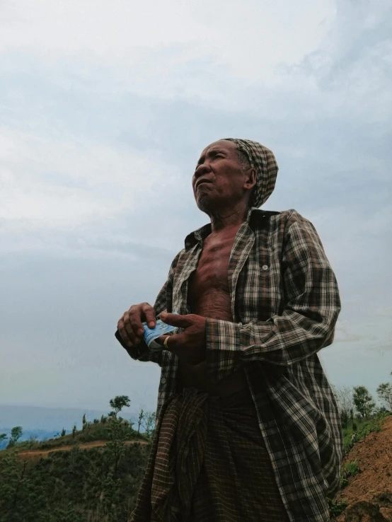 a man standing on top of a lush green hillside, by Ingrida Kadaka, she is holding a smartphone, praying with tobacco, slide show, older woman