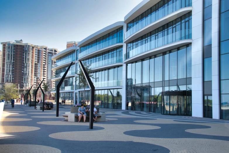 a group of people sitting on a bench in front of a building, full of clear glass facades, at the waterside, steel archways, manuka