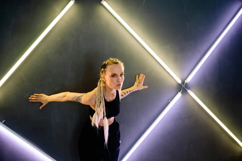 a woman standing in front of a wall with neon lights, inspired by Louisa Matthíasdóttir, pexels contest winner, light and space, die antwoord ( yolandi visser ), arms stretched out, square, evanna lynch