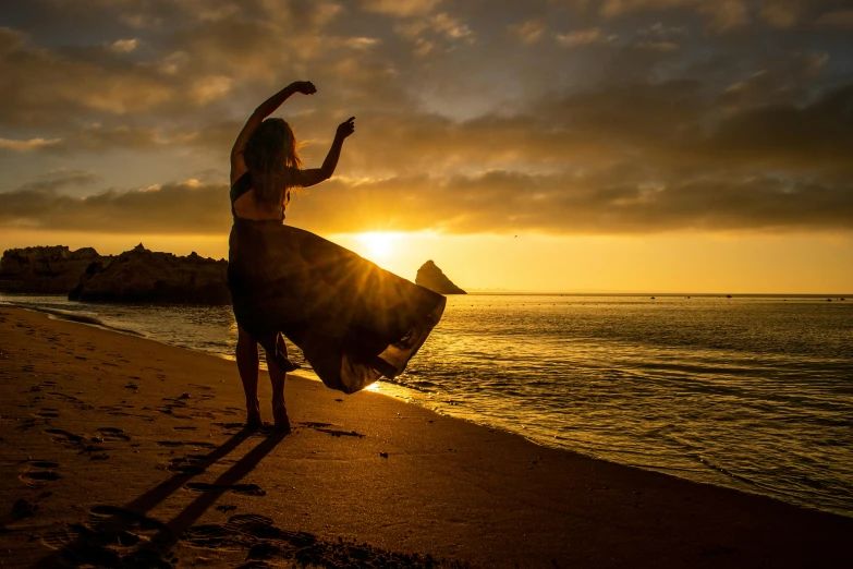 a woman standing on top of a beach next to the ocean, twirly, golden glow, award winning photos, shot with sony alpha