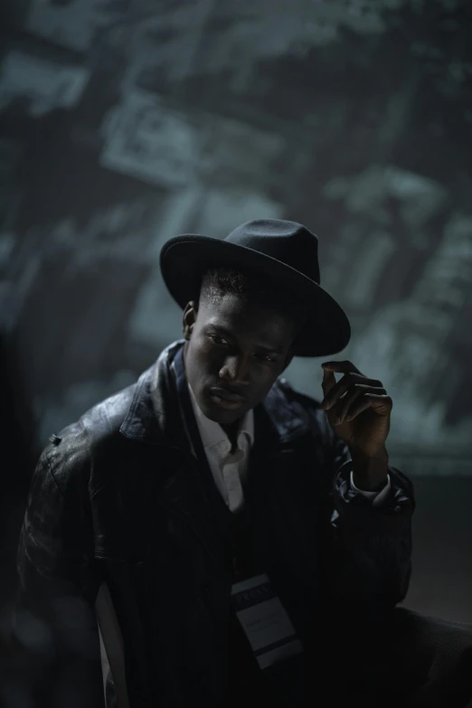 a man sitting in a chair smoking a cigarette, inspired by Gordon Parks, unsplash, harlem renaissance, [ theatrical ], black stetson and coat, standing in a dimly lit room, production photo