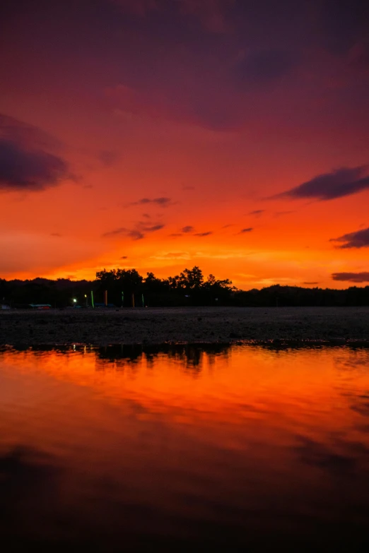 a large body of water with a sunset in the background, the sky is red, on the beach during sunset, riverside, lava reflections