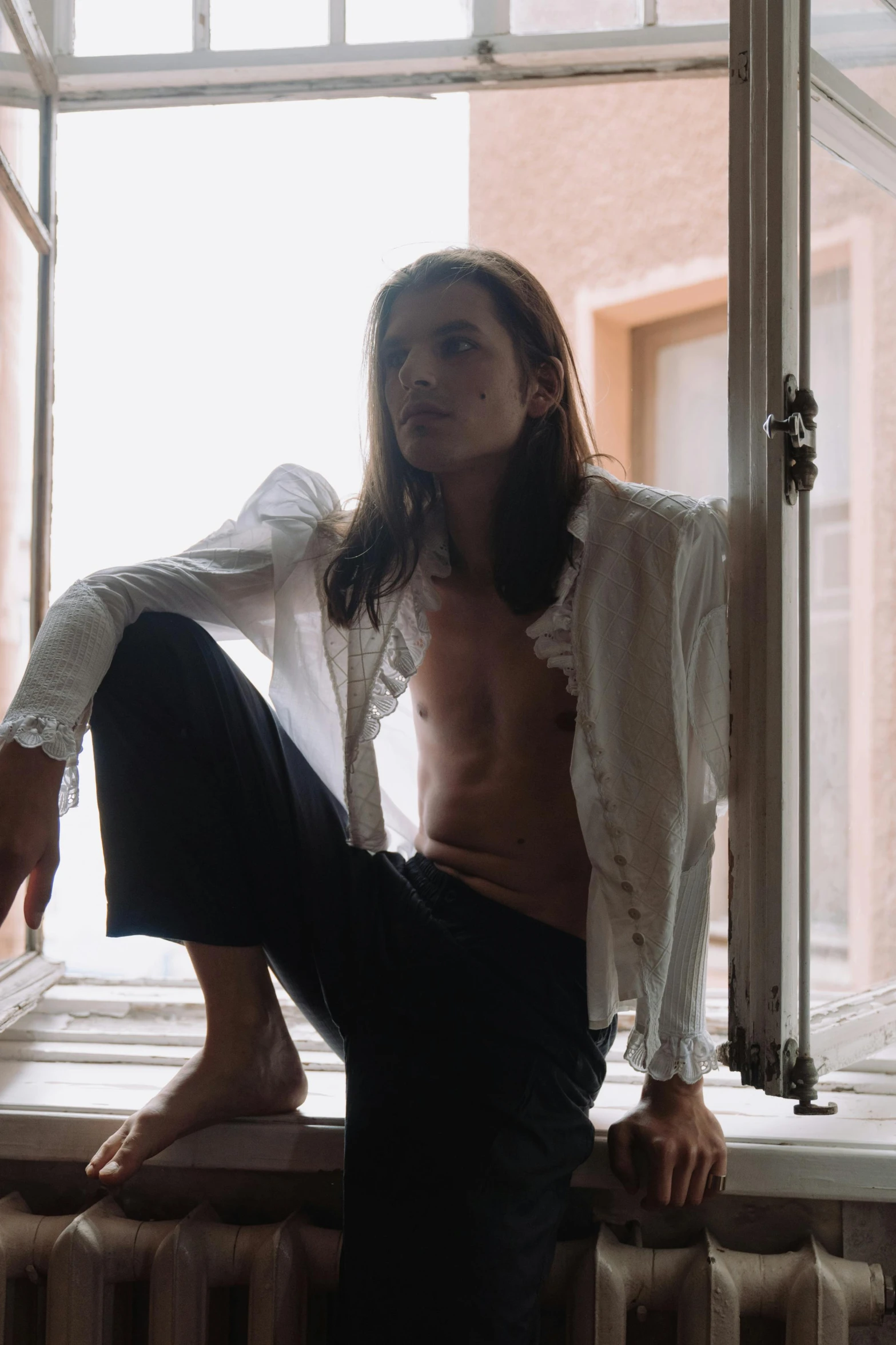 a woman sitting on a window sill next to a radiator, an album cover, inspired by Elsa Bleda, trending on unsplash, renaissance, masculine and handsome, young with long hair, delicate androgynous prince, wearing a white tuxedo