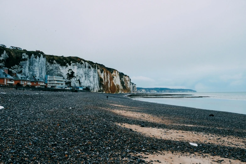 a person standing on a beach next to the ocean, by Rachel Reckitt, pexels contest winner, renaissance, cliffs of dover, traveling in france, gray skies, the village on the cliff