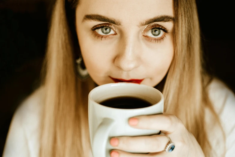 a close up of a person holding a cup of coffee, by Julia Pishtar, trending on pexels, blonde hair and large eyes, girl with dark brown hair, retro stylised, multiple stories