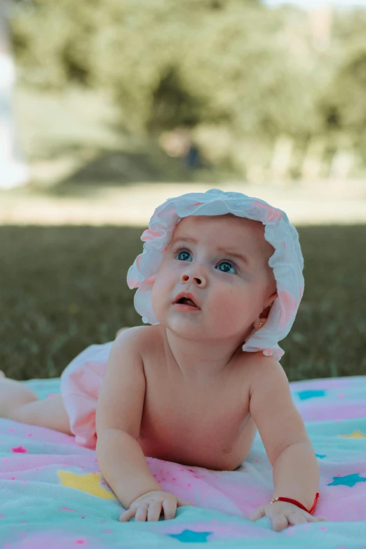 a baby laying on a blanket in the grass, pexels contest winner, shower cap, light pink bikini, she is wearing a hat, pondering