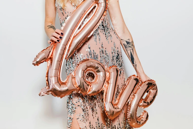 a woman in a dress holding balloons in the shape of the word love, by Julia Pishtar, trending on pexels, rose gold, bottom body close up, official product photo, large tall