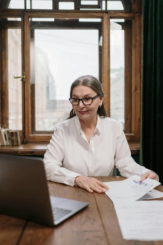 a woman sitting at a table in front of a laptop computer, a portrait, pexels contest winner, white reading glasses, gif, wearing a blouse, documents