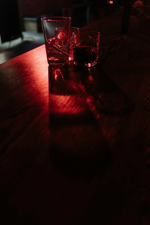 a glass of water sitting on top of a wooden table, inspired by Nan Goldin, unsplash, light and space, detailed red lighting, back lit, saturday night in a saloon, photograph taken in 2 0 2 0