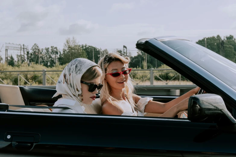 a couple of women that are sitting in a car, by Pamela Ascherson, trending on pexels, fancy dress, convertible, a blond, open road