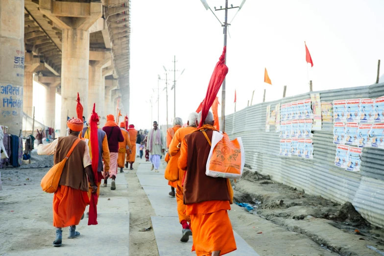 a group of people walking down a sidewalk, samikshavad, wearing red robes, orange line, howrah bridge, hanging