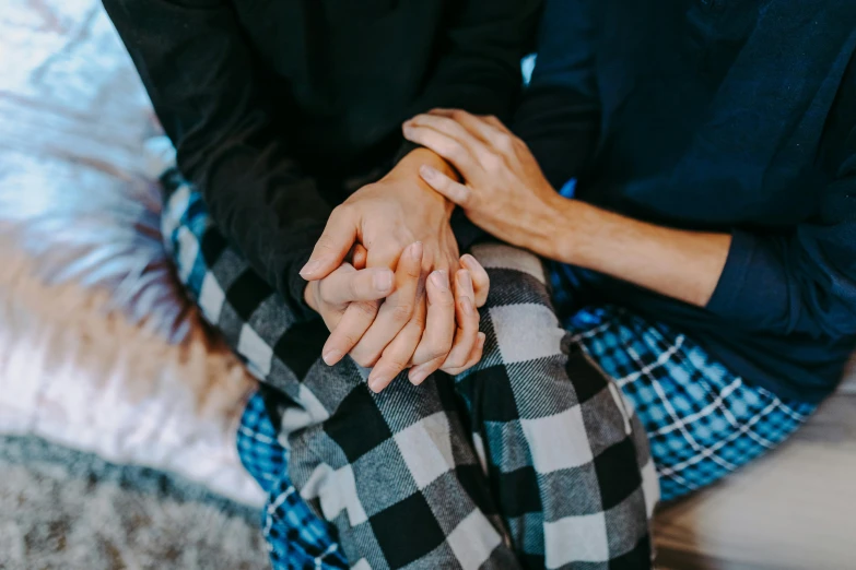 a man and a woman sitting on a bed holding hands, trending on pexels, flannel, compassion, woman holding another woman, patterned