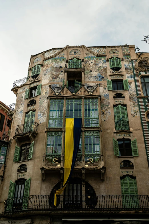 a tall building with lots of windows and green shutters, a mosaic, by Gaudi, unsplash, art nouveau, yellow awning, 2 5 6 x 2 5 6 pixels, photo of poor condition, casually dressed