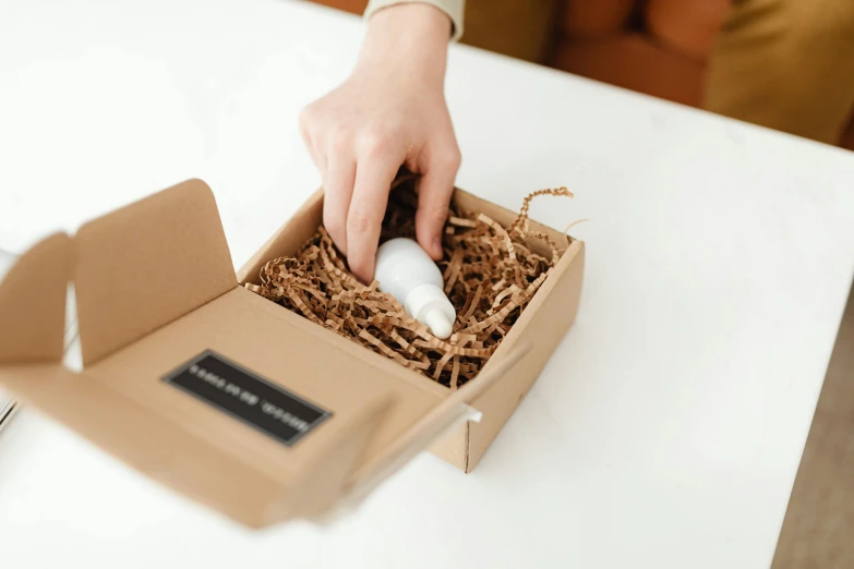 a person putting something in a box on a table, by Eden Box, manuka, skincare, profile image, less detailing