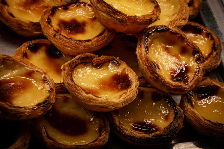 a bunch of pastries sitting on top of a table, by Tom Wänerstrand, pexels, baroque, portugal, flan, charred, full frame image